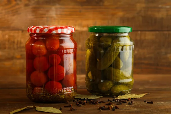 Frascos de pepinos en escabeche y tomates cherry sobre una mesa de madera . —  Fotos de Stock