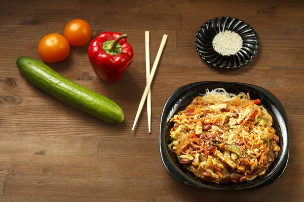 Piatto nero con funchoose e pollo con verdure su un tavolo di legno e verdure fresche . — Foto Stock