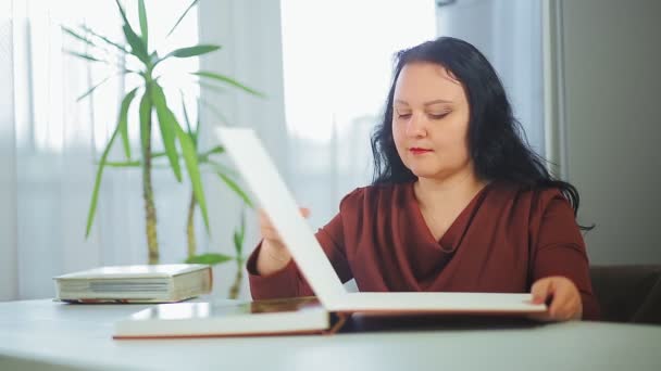 Una mujer está considerando un álbum familiar con fotos en casa . — Vídeos de Stock