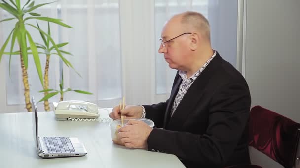 En manlig chef arbetar på ett kontor och äter lunch. — Stockvideo