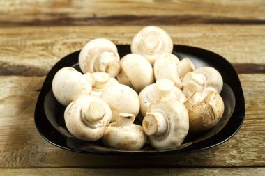 Tahta bir masada siyah tabakta taze şampiyon mantarları..