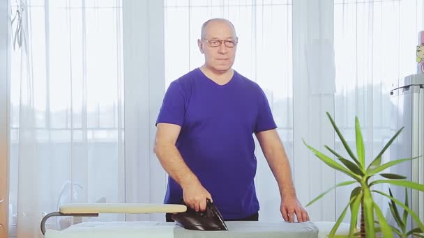 A middle-aged man in the living room ironing clothes on an ironing board. — Stock Video