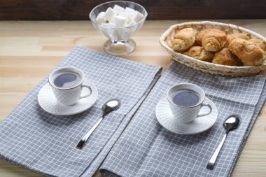 Tahta bir masada, üzerinde kruvasan ve şeker olan peçetelerin üzerinde iki fincan kahve..