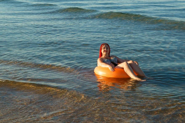 Een jonge vrouw met Afrikaanse staarten ligt te zonnebaden in een rubberen ring in de zee bij de kust.. — Stockfoto