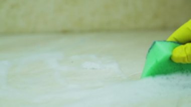 Lastik eldivendeki bir el, süngeri masasının yüzeyinden köpüren bir maddeyle temizler.