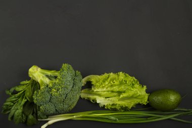 Siyah arka planda yeşil sebze, brokoli, avokado, soğan, ıspanak ve salata..