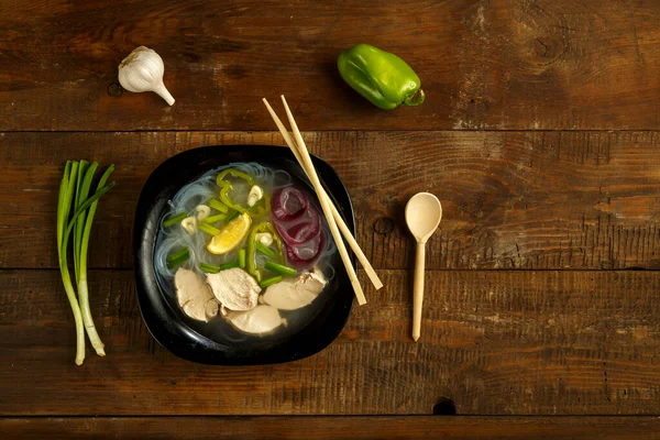 Un plato de sopa Pho vietnamita con pollo en una mesa de madera con una cuchara y palillos . — Foto de Stock