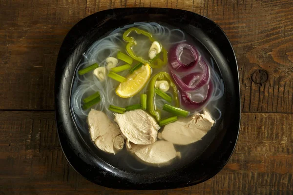 Un plato de sopa pho vietnamita con pollo en una mesa de madera . — Foto de Stock