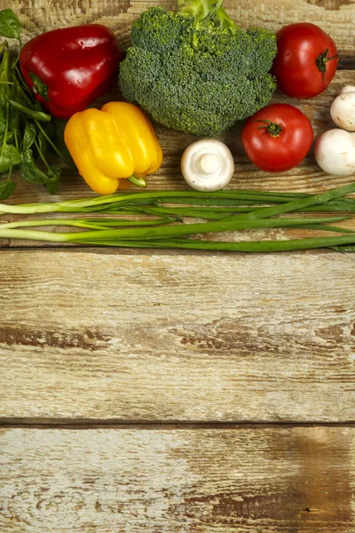 Verduras de brócoli, cebollas verdes, tomates y pimientos, champiñones a lo largo del borde de la mesa de tablas ásperas . — Foto de Stock