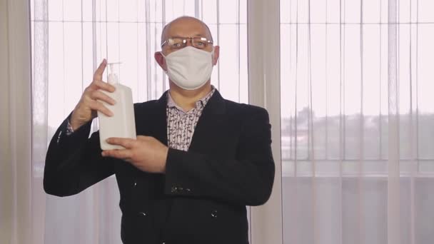 Чоловік у громадському місці в захисній масці дезінфікує руки професійним антисептиком — стокове відео