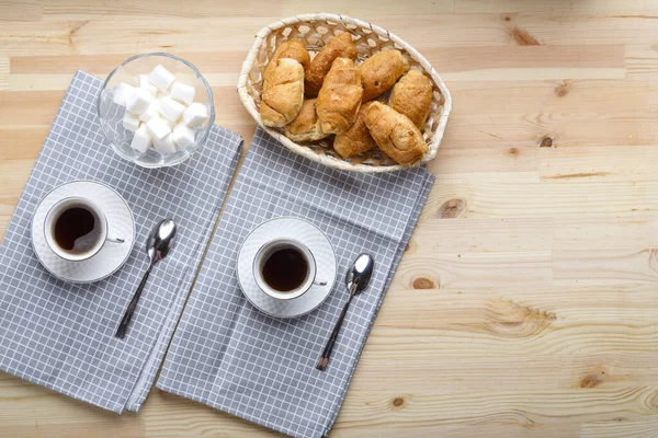 Две чашки кофе на салфетках на деревянном столе с круассанами и вафлями . — стоковое фото