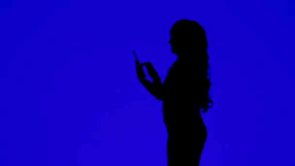 一个身材苗条 一头卷发的女人的轮廓 在蓝色背景的平板上用信使与人交流 总体计划 — 图库视频影像