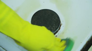Lastik eldivendeki bir el gaz sobasının yüzeyindeki kiri sünger ve deterjanla temizler. Ortalama plan