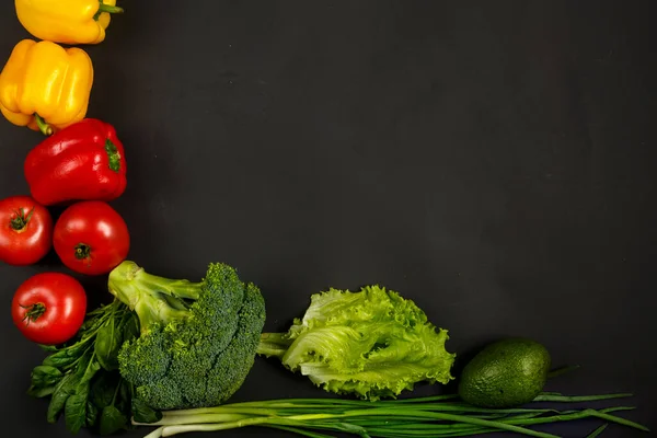 Verduras brillantes coloridas, tomates, pimientos, brócoli, aguacate, cebollas, espinacas y ensalada en el borde de un fondo negro . — Foto de Stock