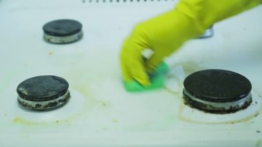 Lastik eldivendeki bir el gaz sobasının yüzeyindeki kiri sünger ve deterjanla temizler..