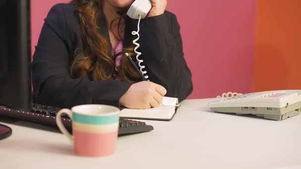 De vrouw in het kantoor spreekt aan de telefoon en schrijft informatie. — Stockvideo