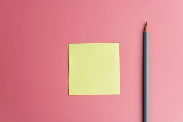 one yellow sticky note reminder and a pencil on a red background