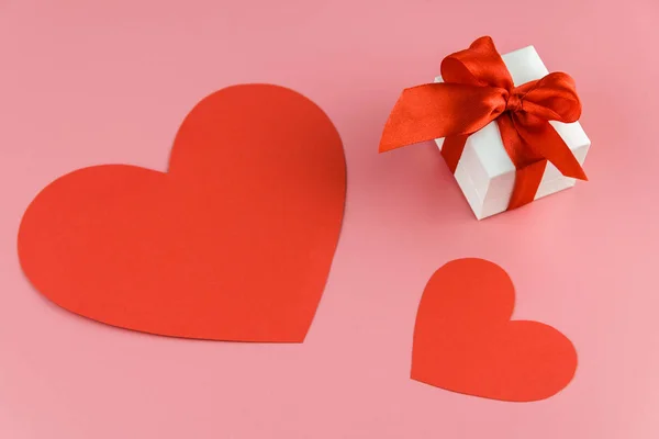 Белый подарочная коробка с красным ремешком и две бумаги, созданные сердца на цветном фоне, обручальное кольцо коробка — стоковое фото
