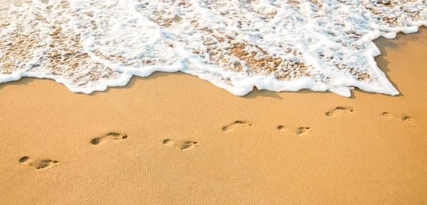 Footprints on a clear sandy beach and a clean white wave — Stock Photo, Image