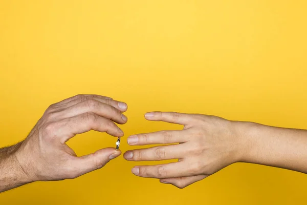 Primer plano de la mano del hombre poniendo un anillo de compromiso en una mano de mujer sobre fondo amarillo — Foto de Stock