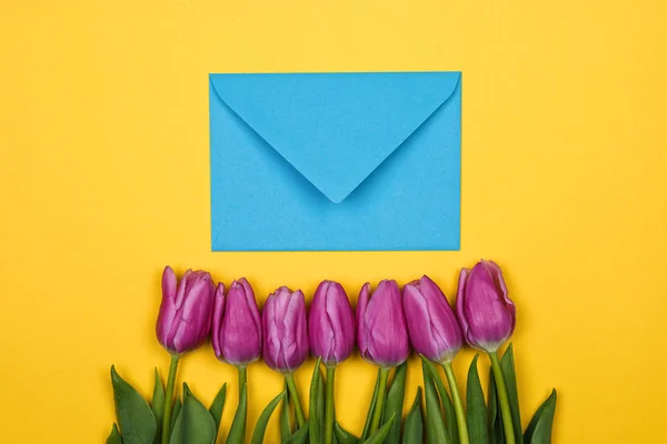 Tulipanes rosados, morados y sobre de coral azul con un corazón rojo sobre fondo amarillo — Foto de Stock