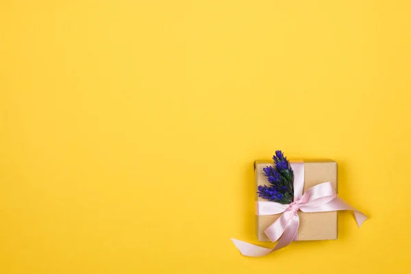 Caja de regalo de papel con un lazo rosa y una ramita de lavanda en la esquina sobre un fondo amarillo con espacio para copiar — Foto de Stock