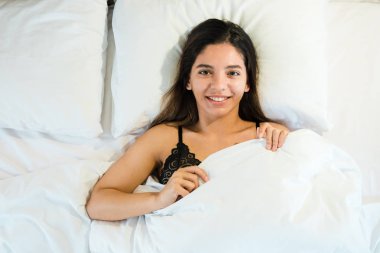 Çekici bir kadın yorganın altında yatıyor ve gülümsüyor.