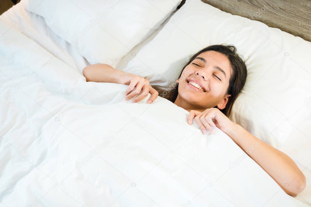 attractive woman lying in the bed underneath white quilt and smiling