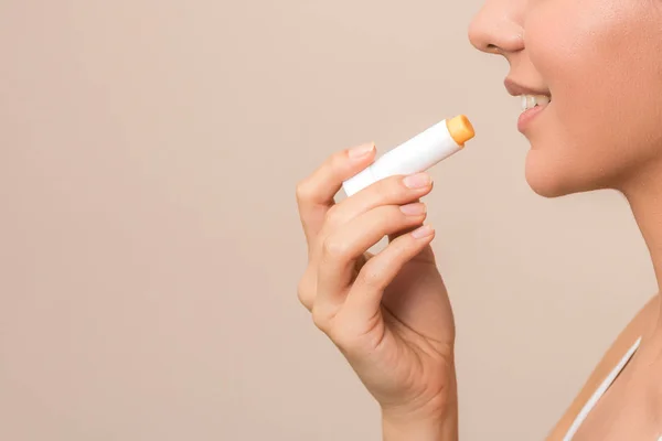 lips care and protection. close up side view of a woman applying balm on lips