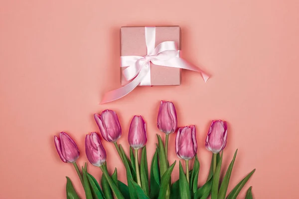 Tulipanes rosados, morados y una pequeña caja de regalo con un lazo sobre fondo rosa. feliz día de las madres — Foto de Stock