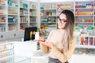 Eczanedeki güzel kadın müşteri elinde beyaz bir kavanozla ilaç tutuyor. Yüzünde bir gülümseme