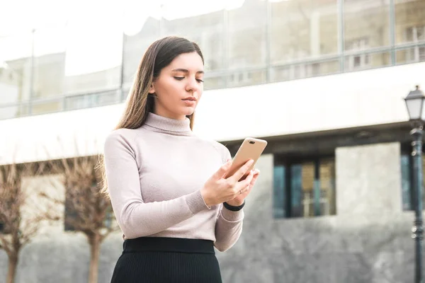 Atractiva mujer de negocios sosteniendo el teléfono móvil y mensaje de texto a su empleado frente al centro de negocios — Foto de Stock