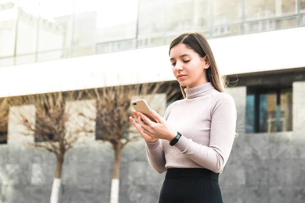 Atractiva mujer de negocios que sostiene el teléfono móvil que busca información en Internet frente al centro de negocios — Foto de Stock