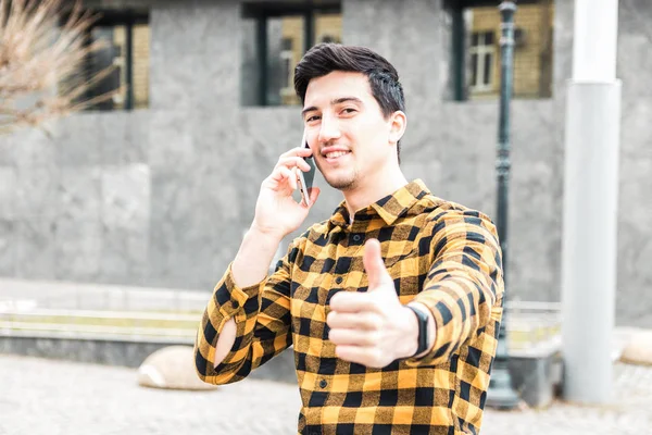 University enrollment. handsome young man or student with smile on face speaking on the phone and showing big thumb up. — Stock Photo, Image