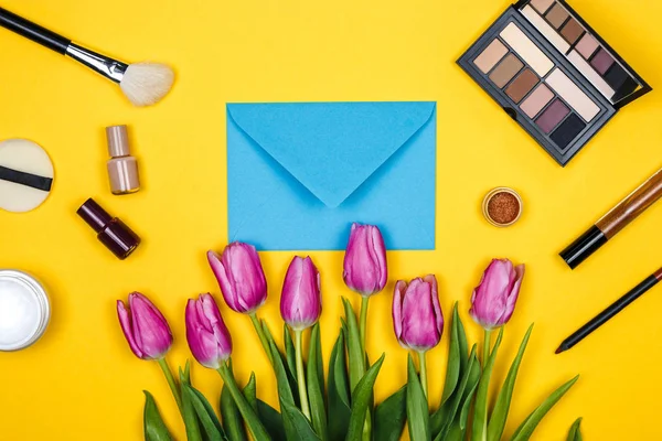 Cosméticos y tulipanes rosados en nackground amarillo y un sobre, cosmético de primavera para las mujeres — Foto de Stock