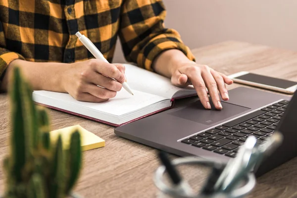 O estudo é poder. fechar as mãos de uma mulher de negócios, estudante ou freelancer em camisa amarela fazendo anotações em seu caderno enquanto navega na internet — Fotografia de Stock