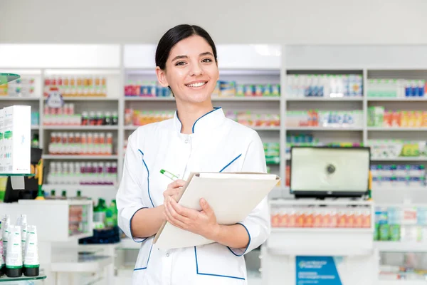 Primer plano farmacéutico con una sonrisa en la cara haciendo notas en la farmacia —  Fotos de Stock
