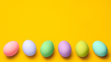 Paskalya yumurtaları, sarı bir zemin üzerine pastel renklerle ve kopyalama uzayı ile boyanmış. Paskalya reklamı Minimalist konsept tasarımı