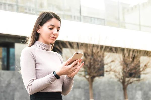 Atractiva mujer de negocios que sostiene el teléfono móvil que busca información en Internet frente al centro de negocios — Foto de Stock