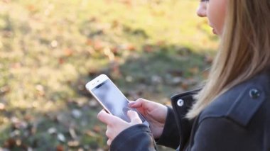 Baharda gün batımında parkta telefonunu kullanan neşeli güzel bir kadının yan görüntüsü.