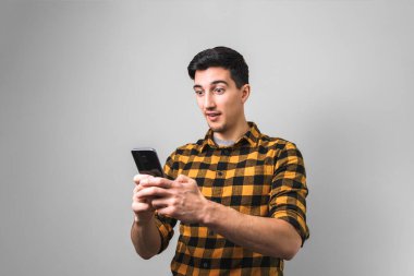 İnanılmaz mutlu haberler. Gri arka planda telefon tutan sarı tişörtlü adam şaşırdı.