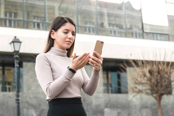 Atractiva mujer de negocios que sostiene el teléfono móvil que busca información en Internet frente al centro de negocios — Foto de Stock