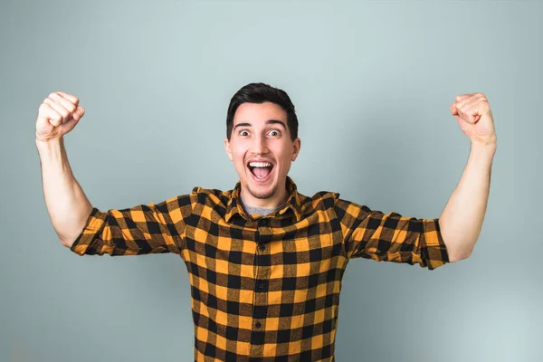 Winner in life. happily excited handsome man with nice smile in yellow shirt with both arms raised up on grey background. — Stock Photo, Image