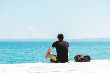 Yanında sırt çantasıyla yalnız gezen genç adam meditasyon yapıyor okyanusa bakıyor ve sessizliğin tadını çıkarıyor.