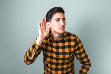 Sarı tişörtlü yakışıklı genç, izole edilmiş gri arka planda bir şeyler duymaya çalışıyor.