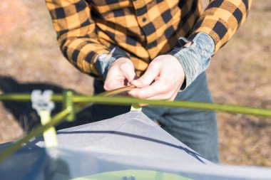 Sarı gömlekli adam baharda dağlarda çadır kuruyor.