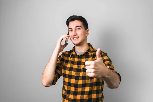 University enrollment. handsome young man or student with smile on face speaking on the phone and showing big thumb up — Stock Photo, Image
