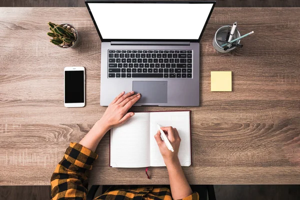 Vista superior mãos femininas usando um laptop e escrever em notebook. telefone e notas pegajosas na mesa — Fotografia de Stock