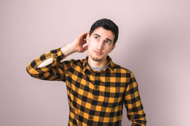 Sarı tişörtlü iyi görünümlü bir adam kafasını kaşıyıp yukarı bakarken düşünüyor.