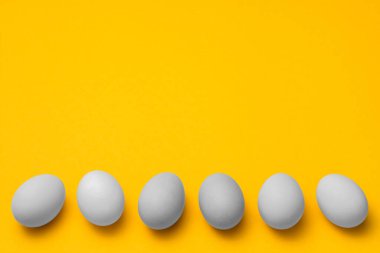 Sarı arka planda arka arkaya beyaz yumurtalar ve kopyasal alan. Paskalya minimalist konsept tasarımı